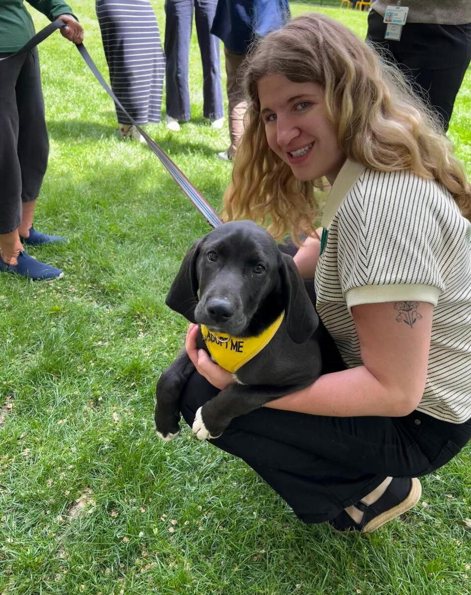 woman crouches down with black puppy